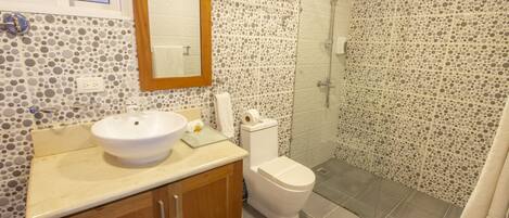 A bathroom with a round sink, wooden cabinets, a toilet, and a shower area.