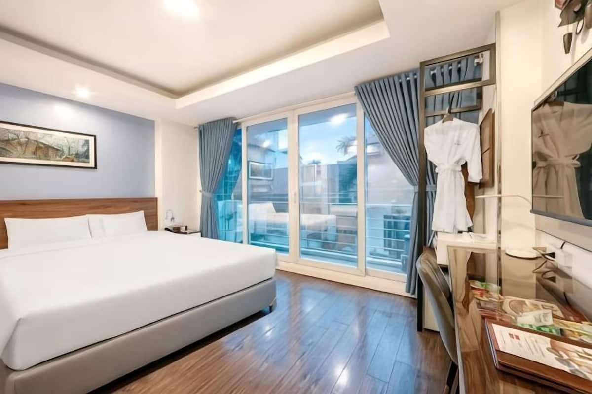A hotel room with a large bed, a balcony with a view, and a robe rack.