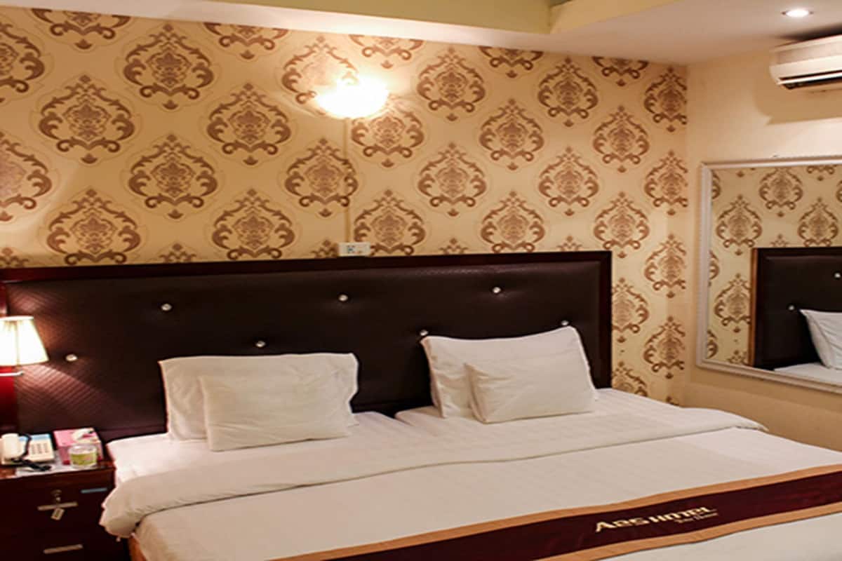 A hotel room with a large bed, a headboard with buttons, a bedside lamp, and a mirror on the wall.