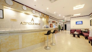 Zona de recepció amb mostrador de marbre, dues banquettes, televisió i zona de seients amb sofàs i taula.