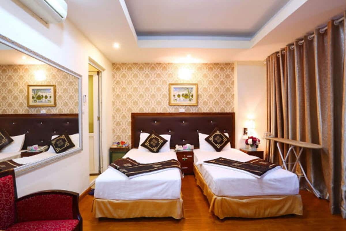 A hotel room with two beds, a mirror, a red chair, and a window with curtains.