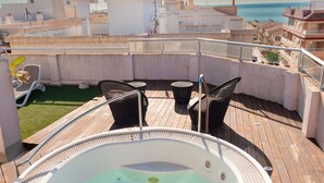 A rooftop with a hot tub, outdoor seating, and a view of the sea.