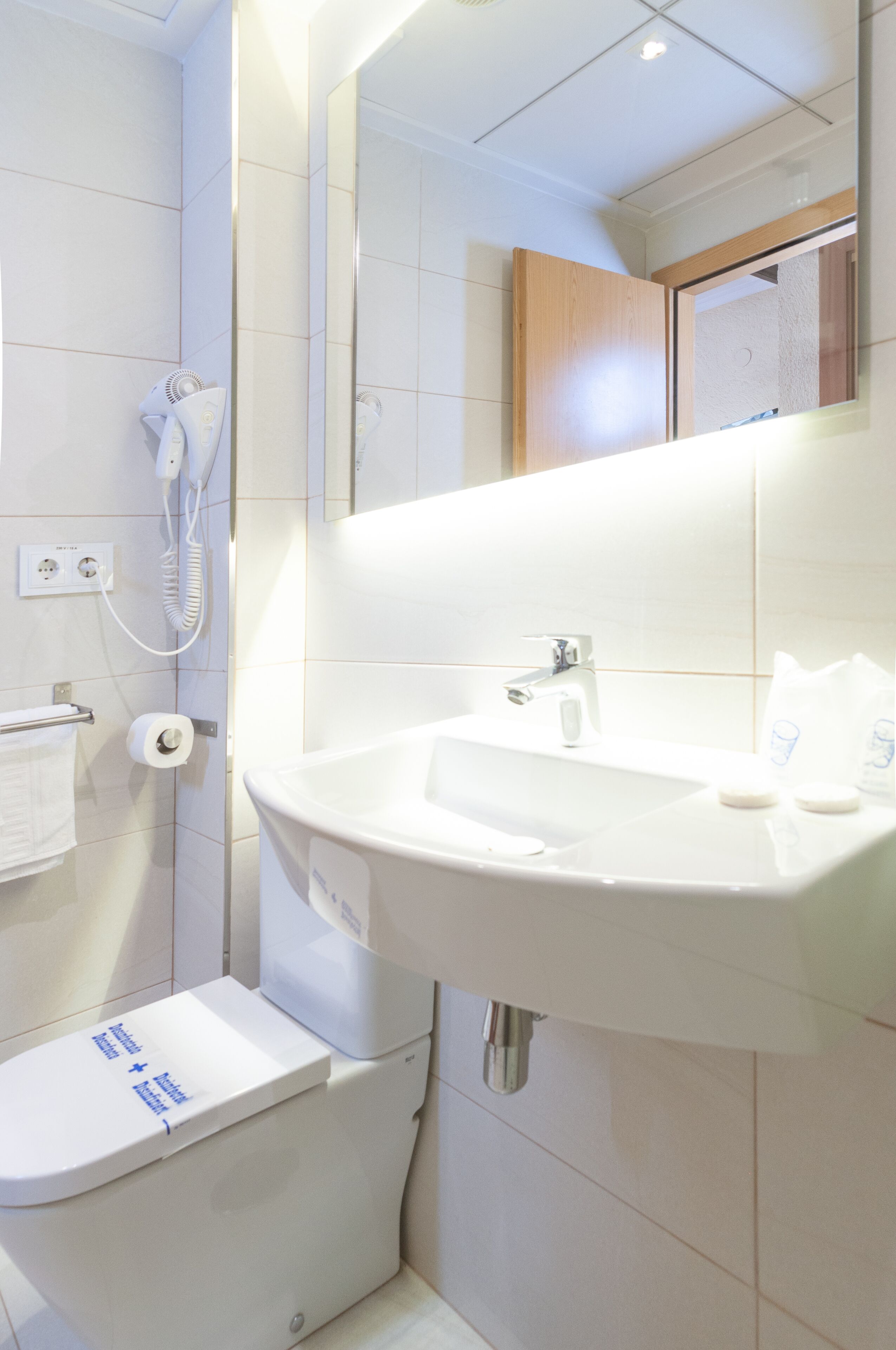 Een badkamer met een wit wastafelmeubel, een spiegel, een toilet en een haardroger aan de muur.