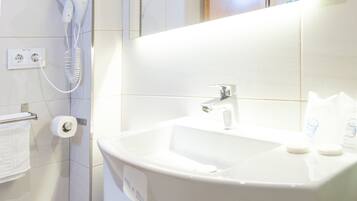 Een badkamer met een wit wastafelmeubel, een spiegel, een toilet en een haardroger aan de muur.