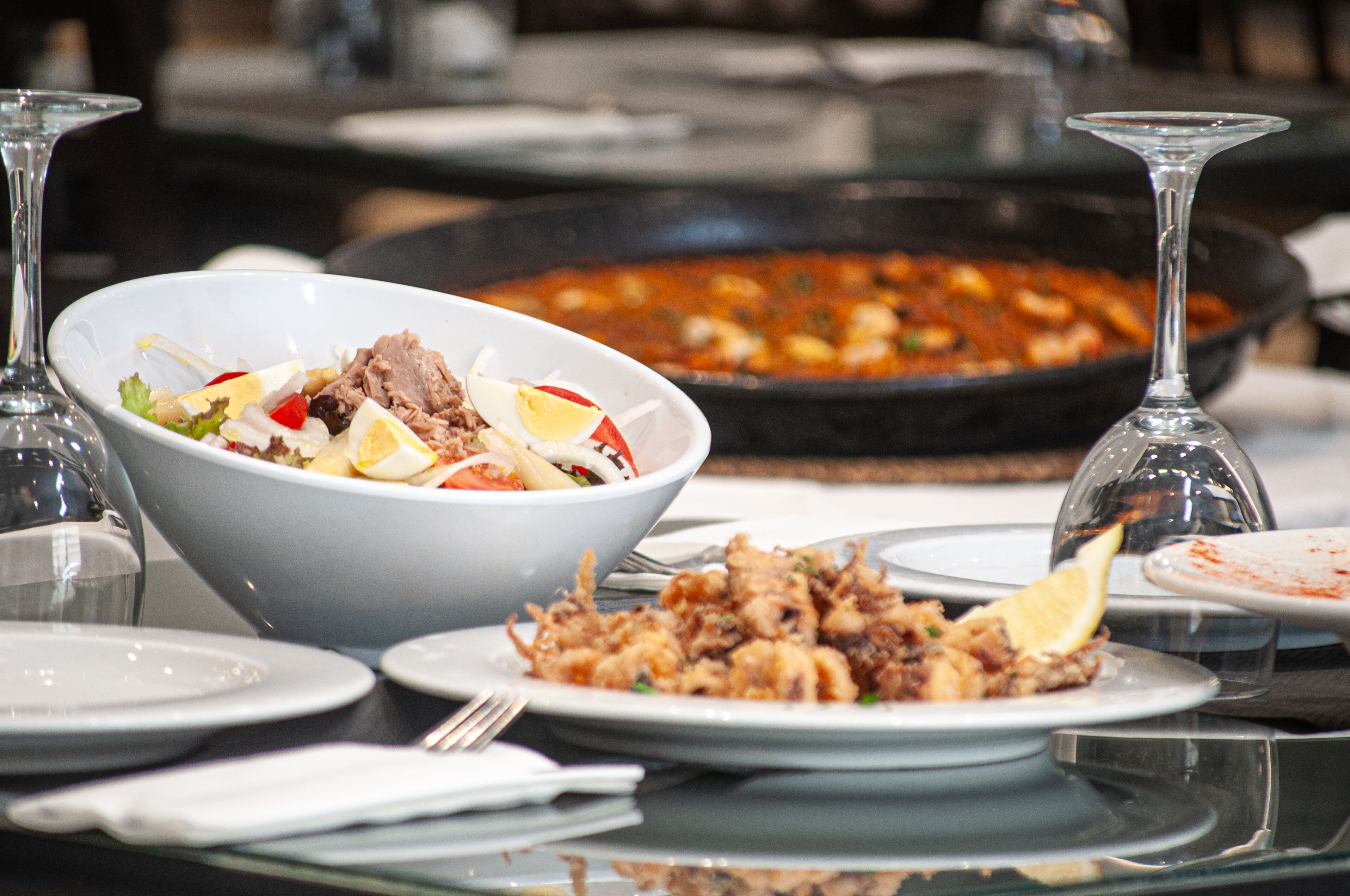 A dining table with a bowl of salad, a plate of fried food, and a pan of stew.