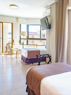 Habitación de hotel con dos camas, un escritorio, una silla, un televisor montado en la pared y una ventana con vistas a edificios.