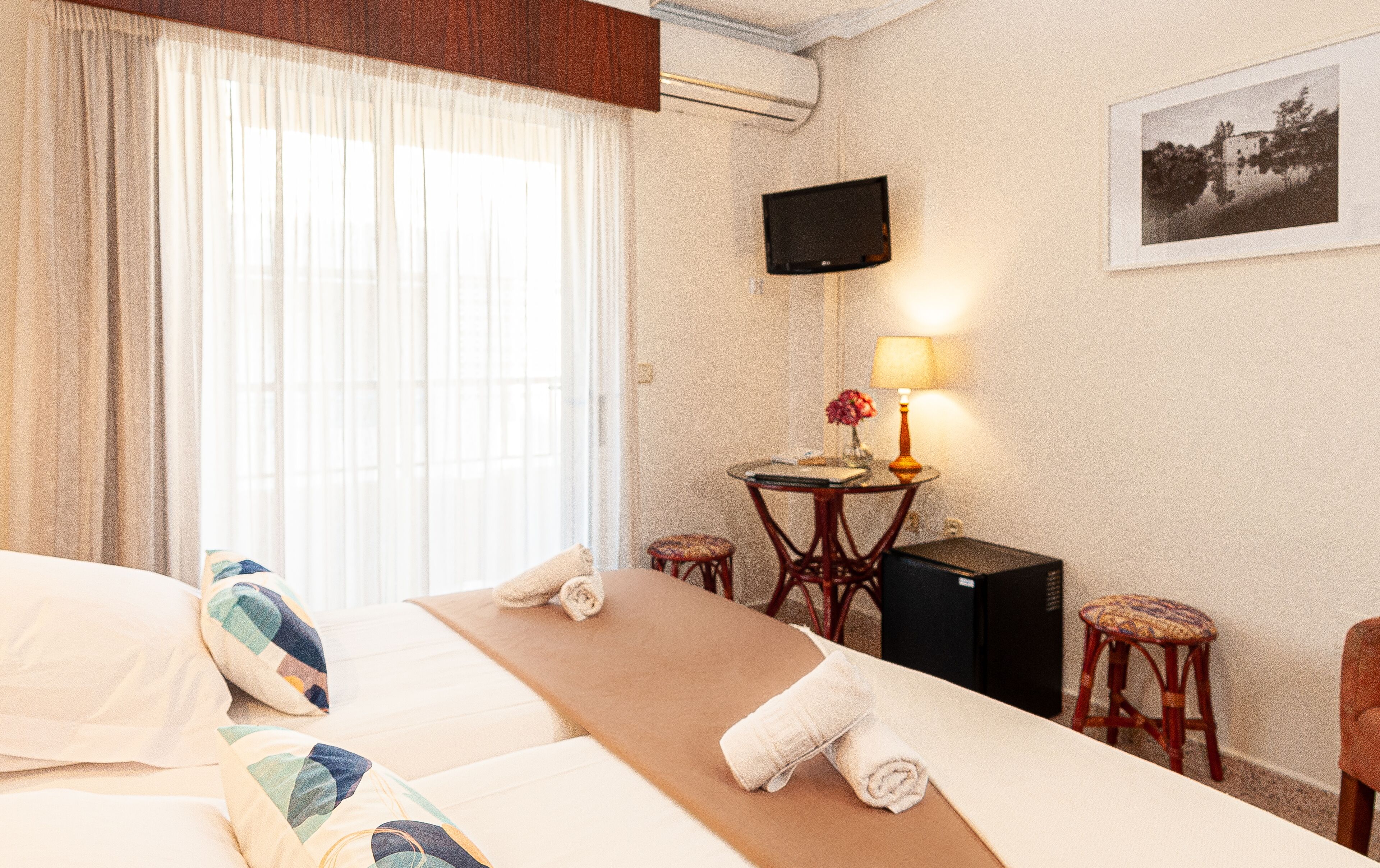 A hotel room with a bed, a desk with a lamp, a chair, and a TV on the wall.