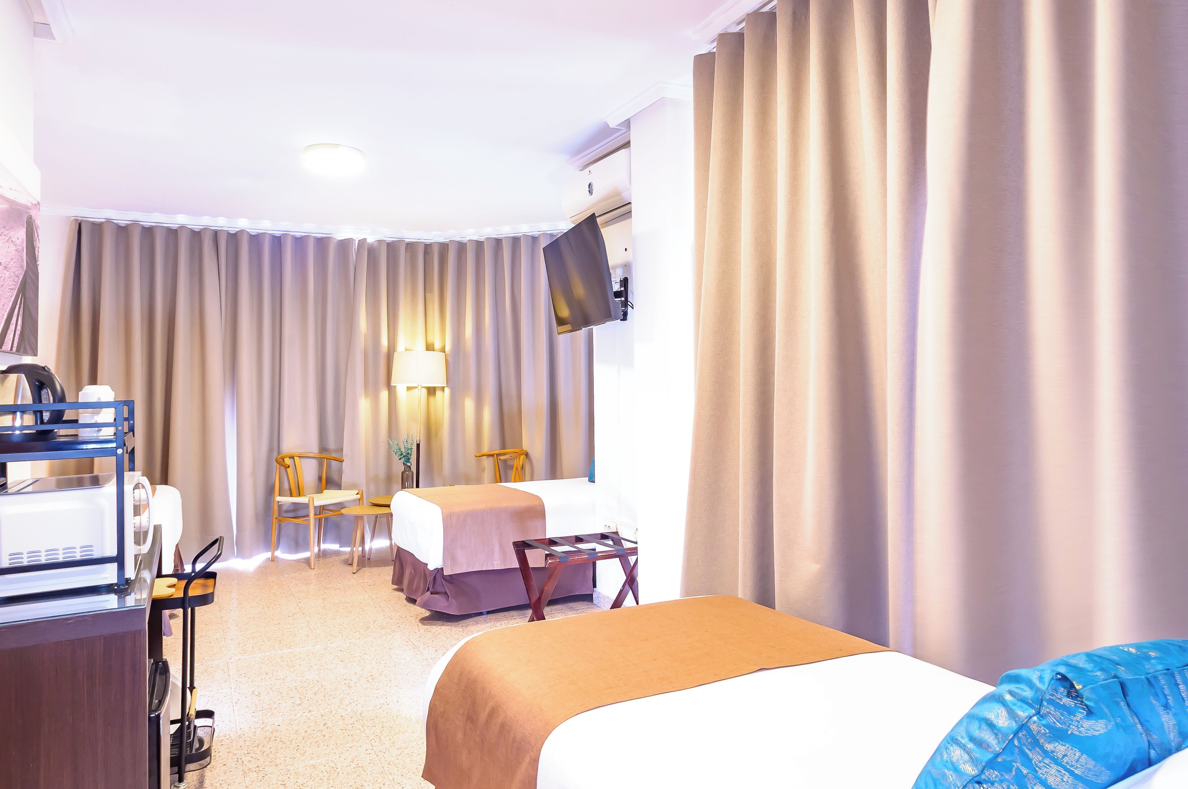 A hotel room with a bed, a desk, a chair, a TV, and curtains.