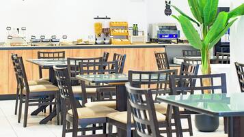 Un restaurant amb taules i cadires de fusta, una barra amb maquinària de cuina i una planta verda gran.