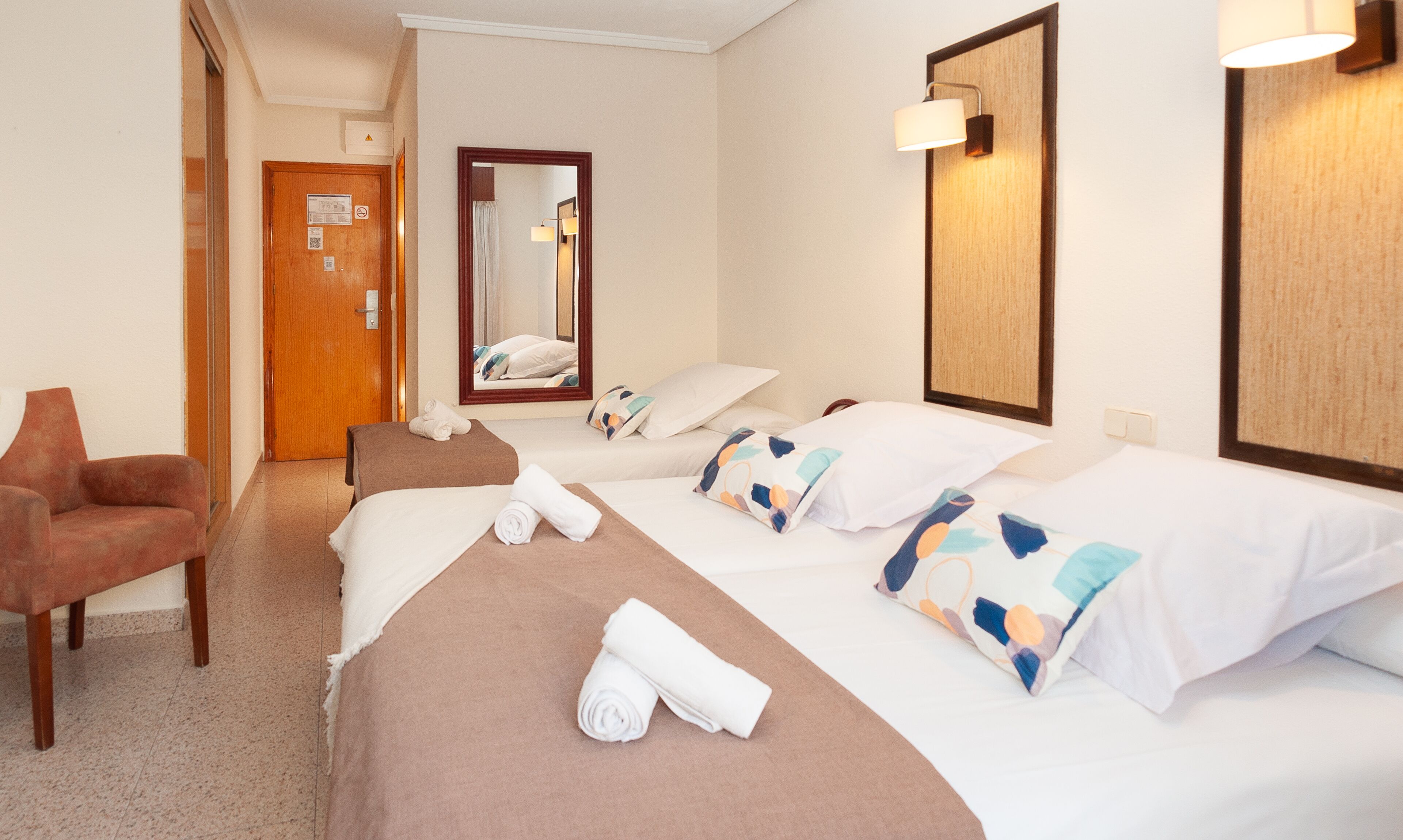 Una habitación de hotel con una cama, una silla, un espejo y una puerta.