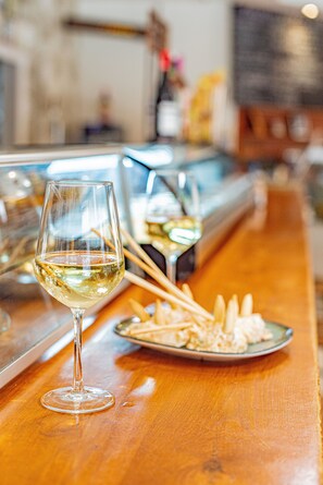 Una copa de vino blanco sobre una barra de madera, con un plato de comida y palillos.