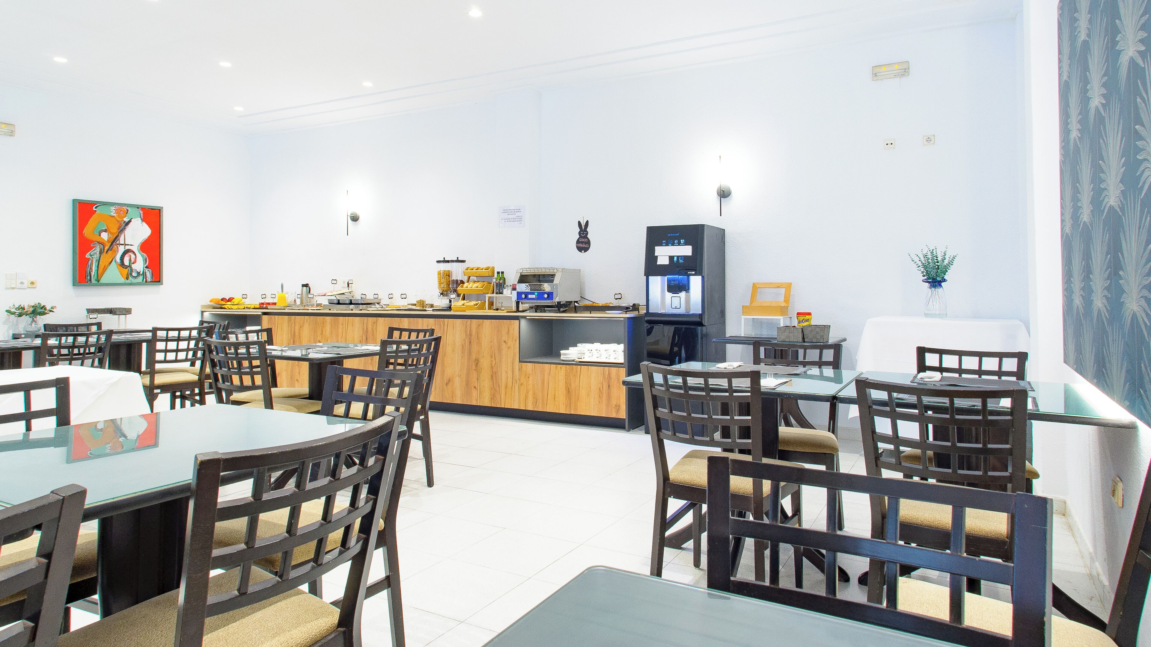 Un restaurante con mesas y sillas de madera, una barra con una máquina de café y un cuadro en la pared.