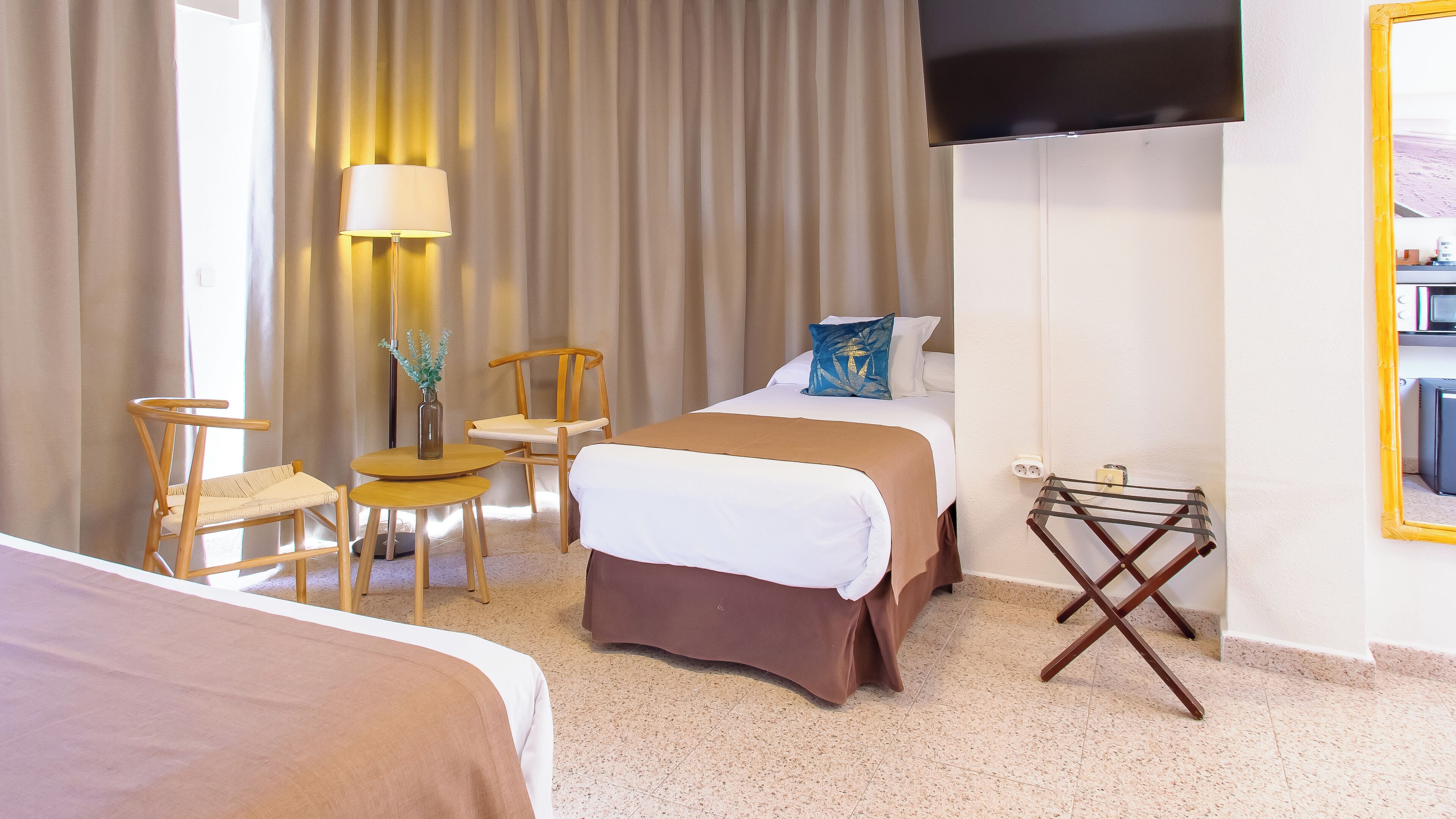 Een hotelkamer met een bed, een stoel, een tafeltje, een lamp en een aan de muur bevestigde televisie.