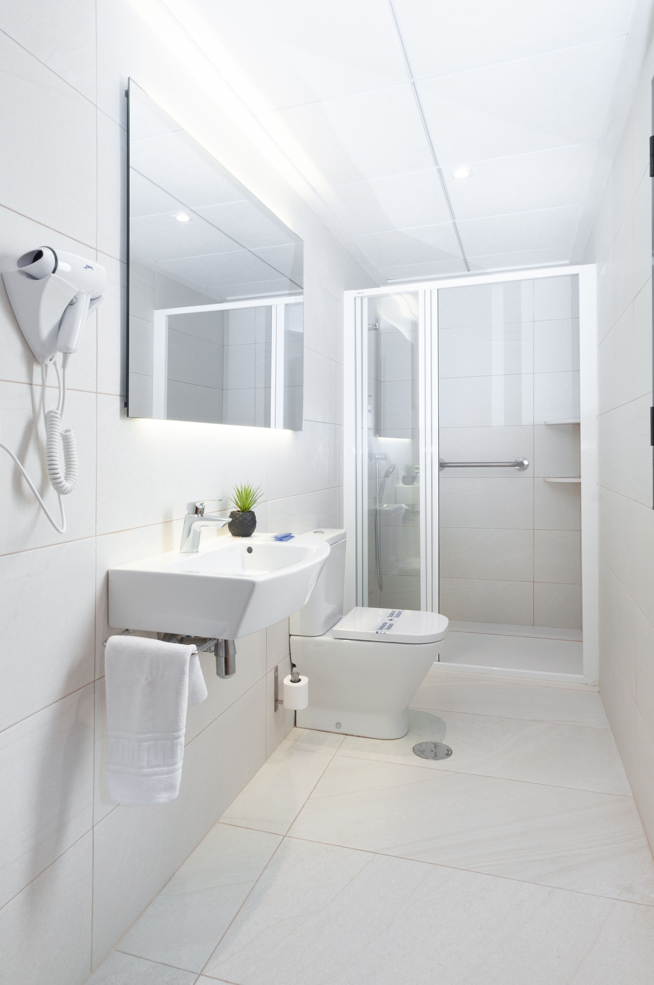 Un baño moderno con lavamanos, espejo y retrete blancos.