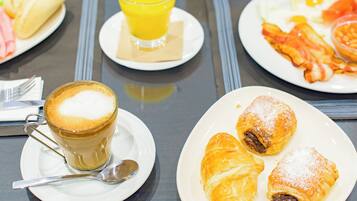 Un desayuno con una taza de café, cruasanes y un plato de huevos y tocino.