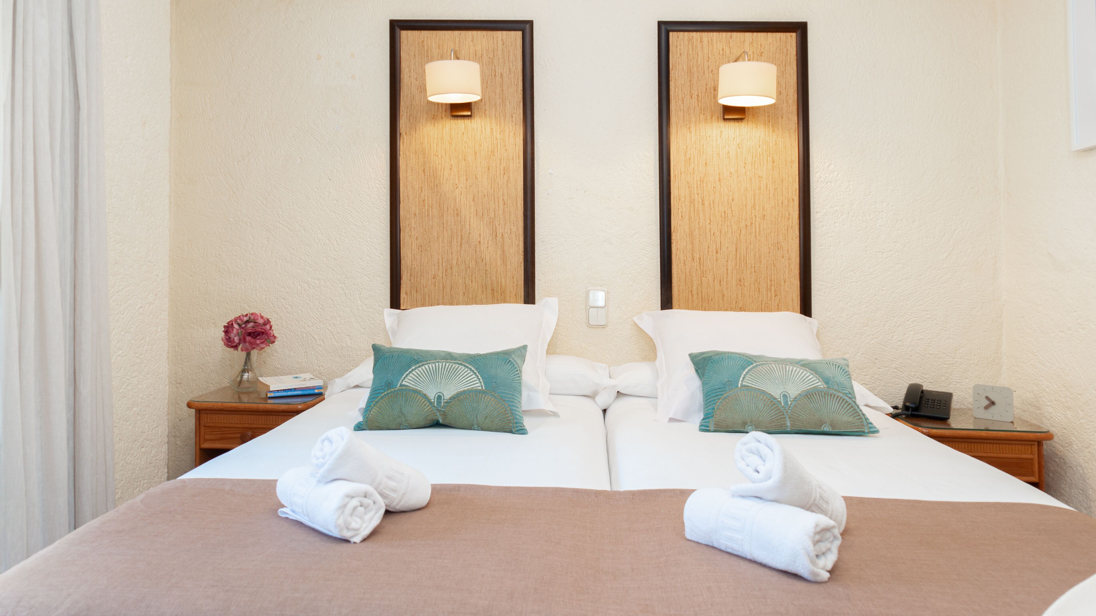 A double bed with two pillows, a bedside table with a lamp, a clock, and a phone.