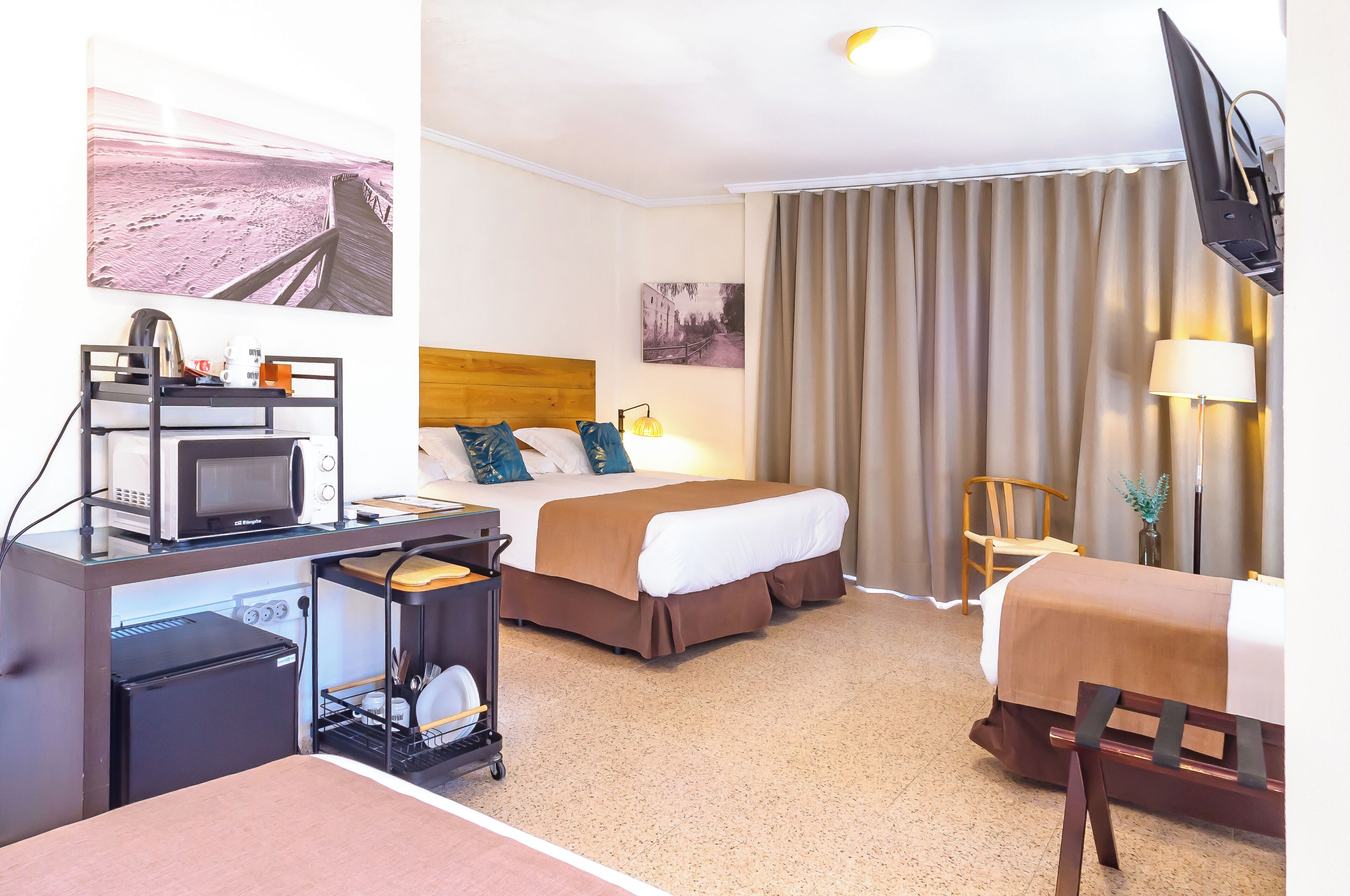 Ein Hotelzimmer mit einem Bett, einem Schreibtisch mit Mikrowelle, einem kleinen Kühlschrank, einem Sessel, einem Fernseher und einem Fenster mit Vorhängen.