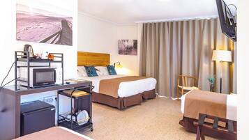 Ein Hotelzimmer mit einem Bett, einem Schreibtisch mit Mikrowelle, einem kleinen Kühlschrank, einem Sessel, einem Fernseher und einem Fenster mit Vorhängen.