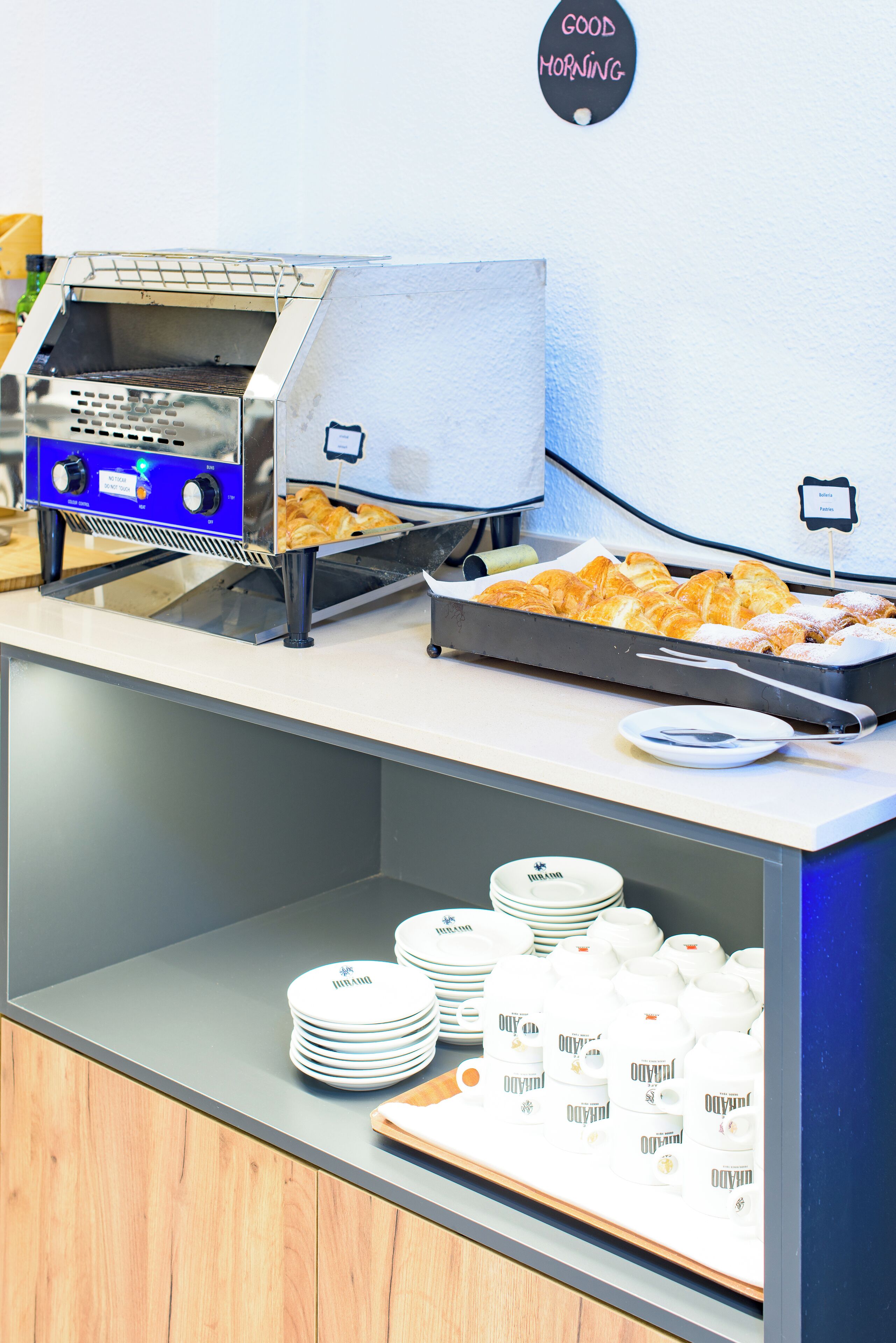 Montaje de bufé con una parrilla, fuentes de comida y platos y recipientes apilados.