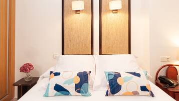 Habitación de hotel con cama, dos lámparas de pared, un florero con flores, un teléfono y una pequeña mesa.
