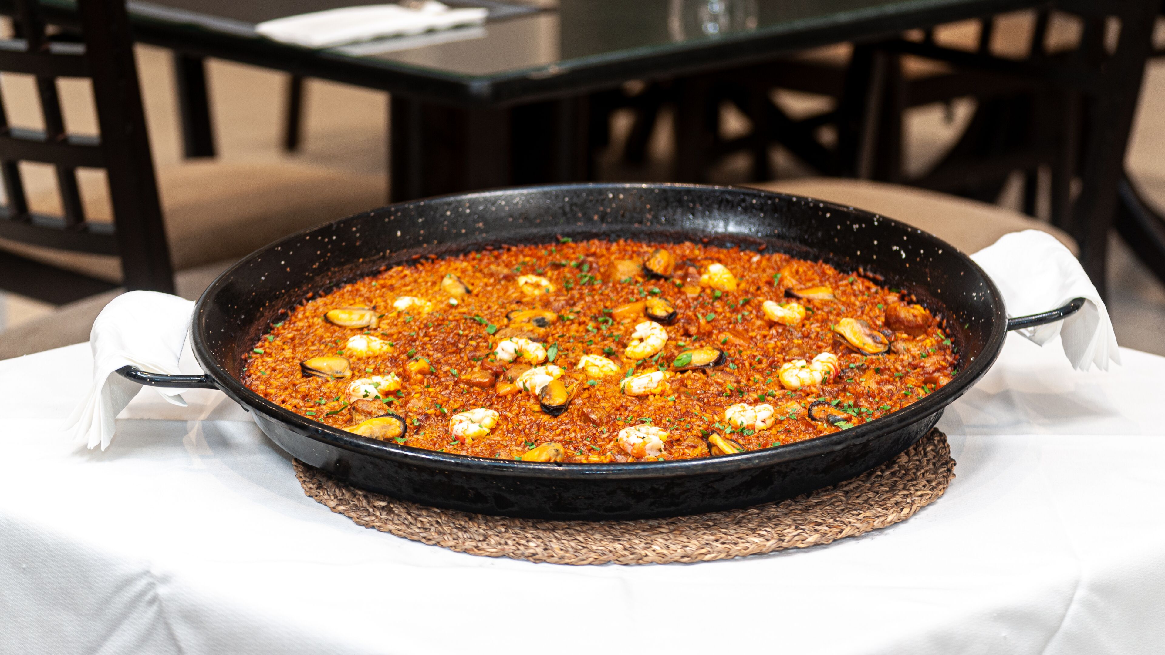 Une grande poêle noire remplie de paella aux fruits de mer, posée sur une nappe blanche.
