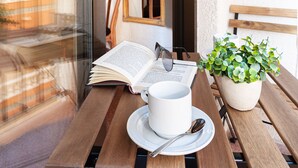 A wooden table with a white cup, saucer, and spoon, an open book, and a potted plant.