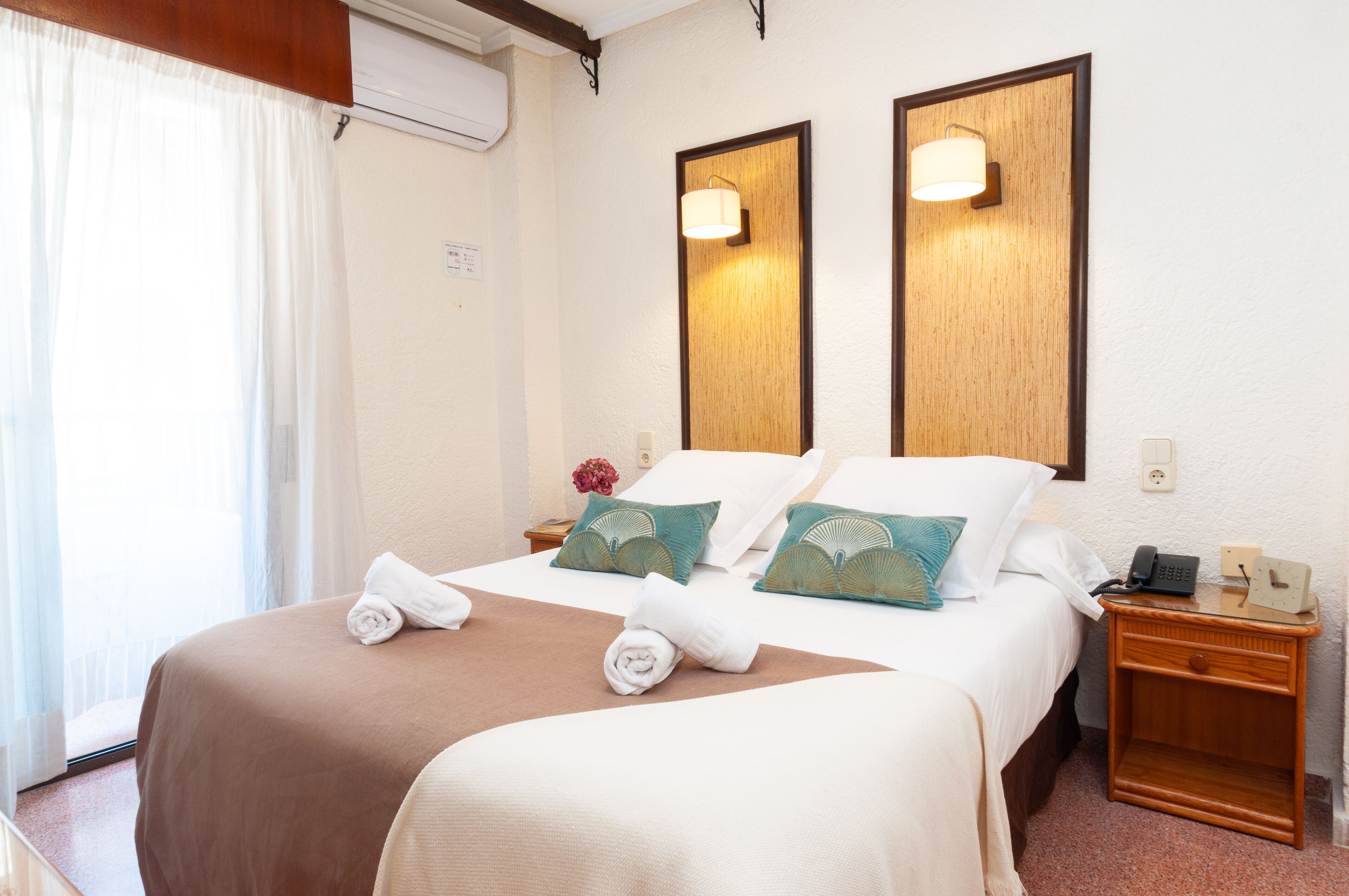 A hotel room with a bed, two bedside lamps, a nightstand, and a telephone.
