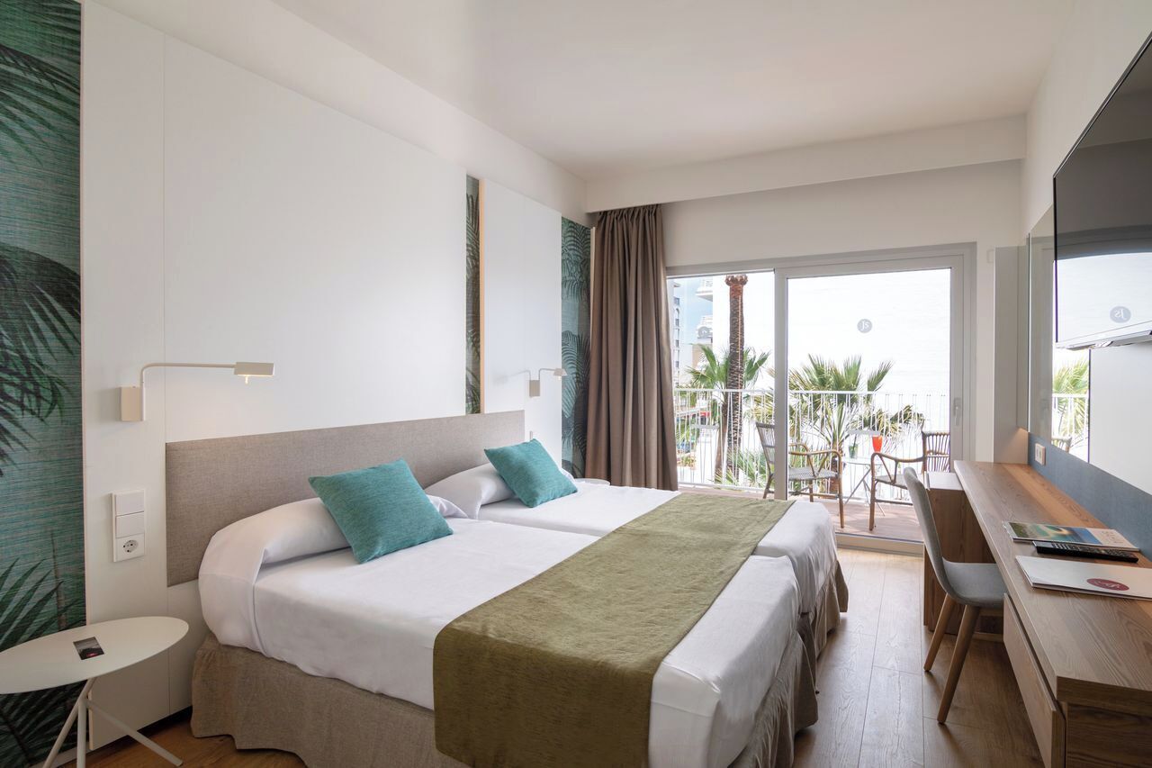 Ein Hotelzimmer mit zwei Betten, einem Schreibtisch, einem Stuhl, einem kleinen Tisch und einem Balkon mit Blick.