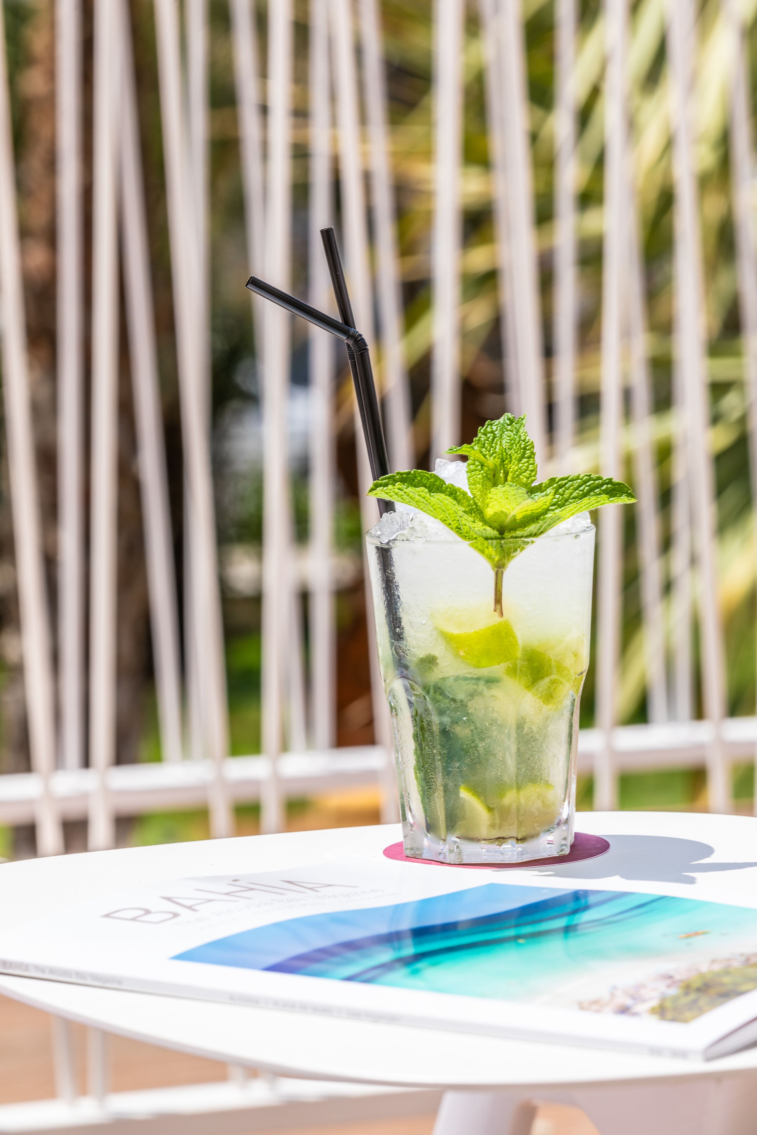 A glass of iced drink with mint leaves and lime, placed on a white table with a magazine.