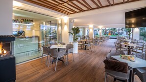 Un amplio comedor interior con suelo de madera, mesas y sillas. Cuenta con una chimenea y una planta grande en maceta.