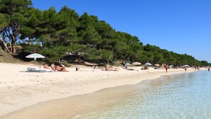 Una playa con aguas transparentes y poco profundas, gente tomando el sol y sombrillas.
