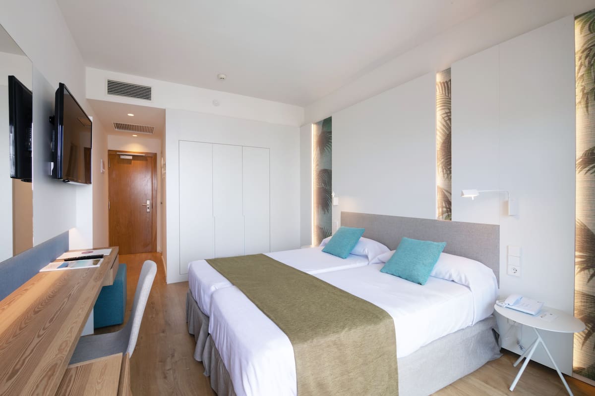 Une chambre d’hôtel moderne équipée d’un lit, d’une table de chevet, d’une chaise et d’un téléviseur fixé au mur.