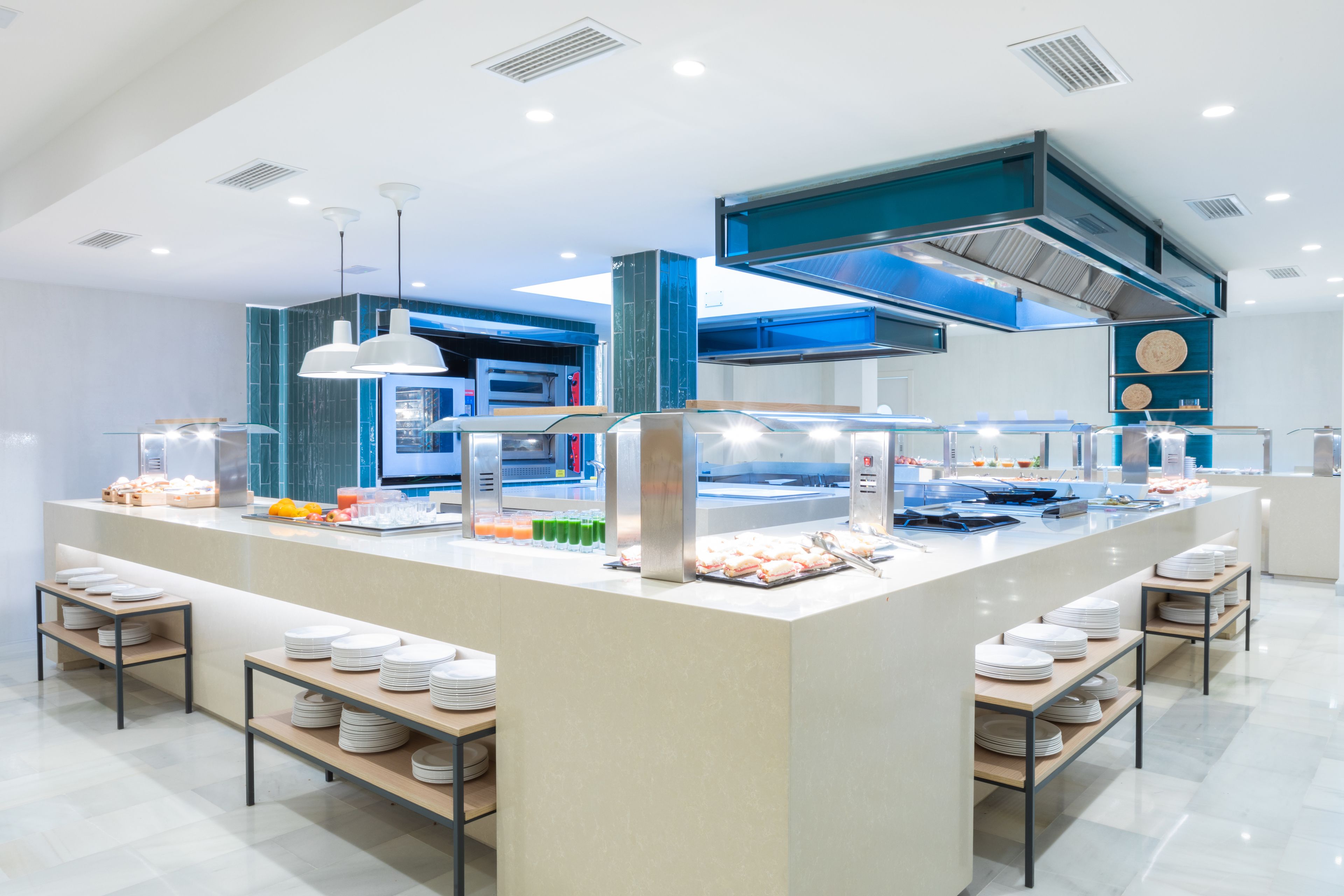 A modern buffet setup with multiple serving stations, a central island, and a kitchen area in the background.