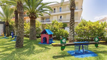 A playground with a seesaw, a small blue house, and palm trees.