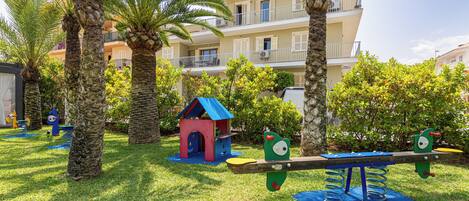 A playground with a seesaw, a small blue house, and palm trees.