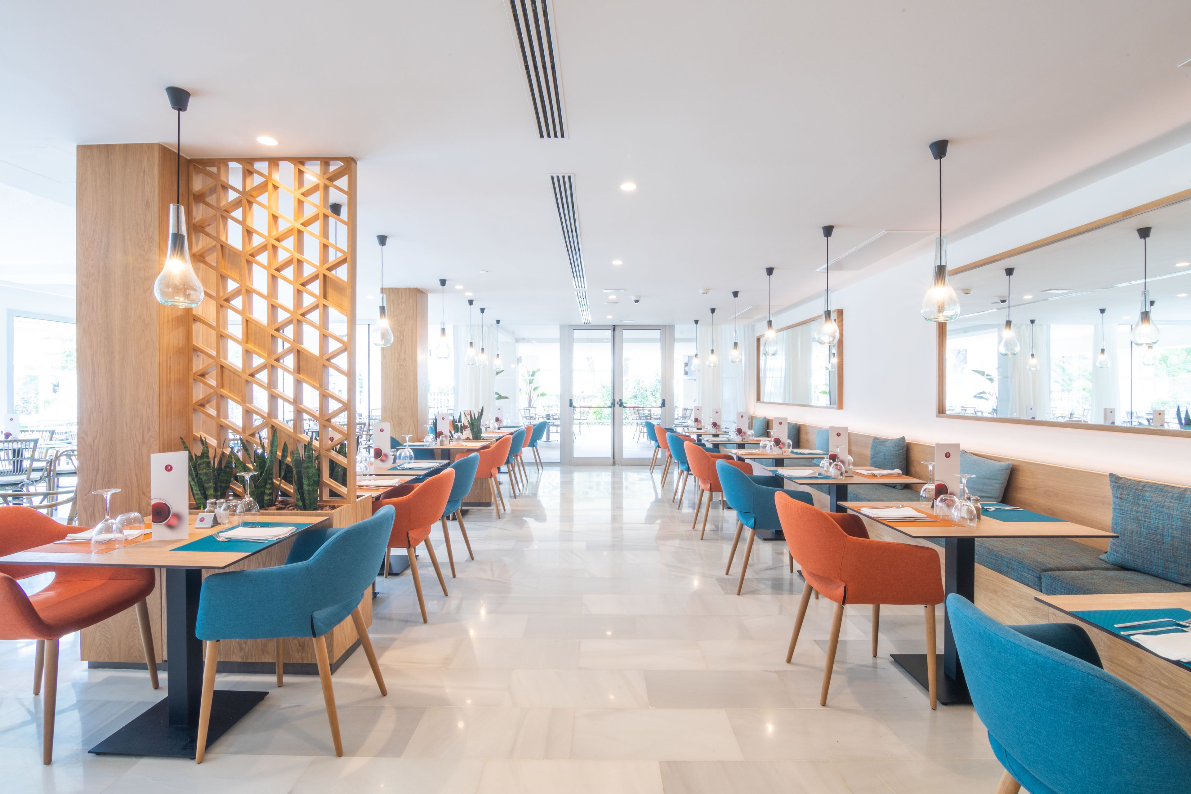 A modern restaurant with a central open space, wooden partitions, and a mix of orange and blue chairs.