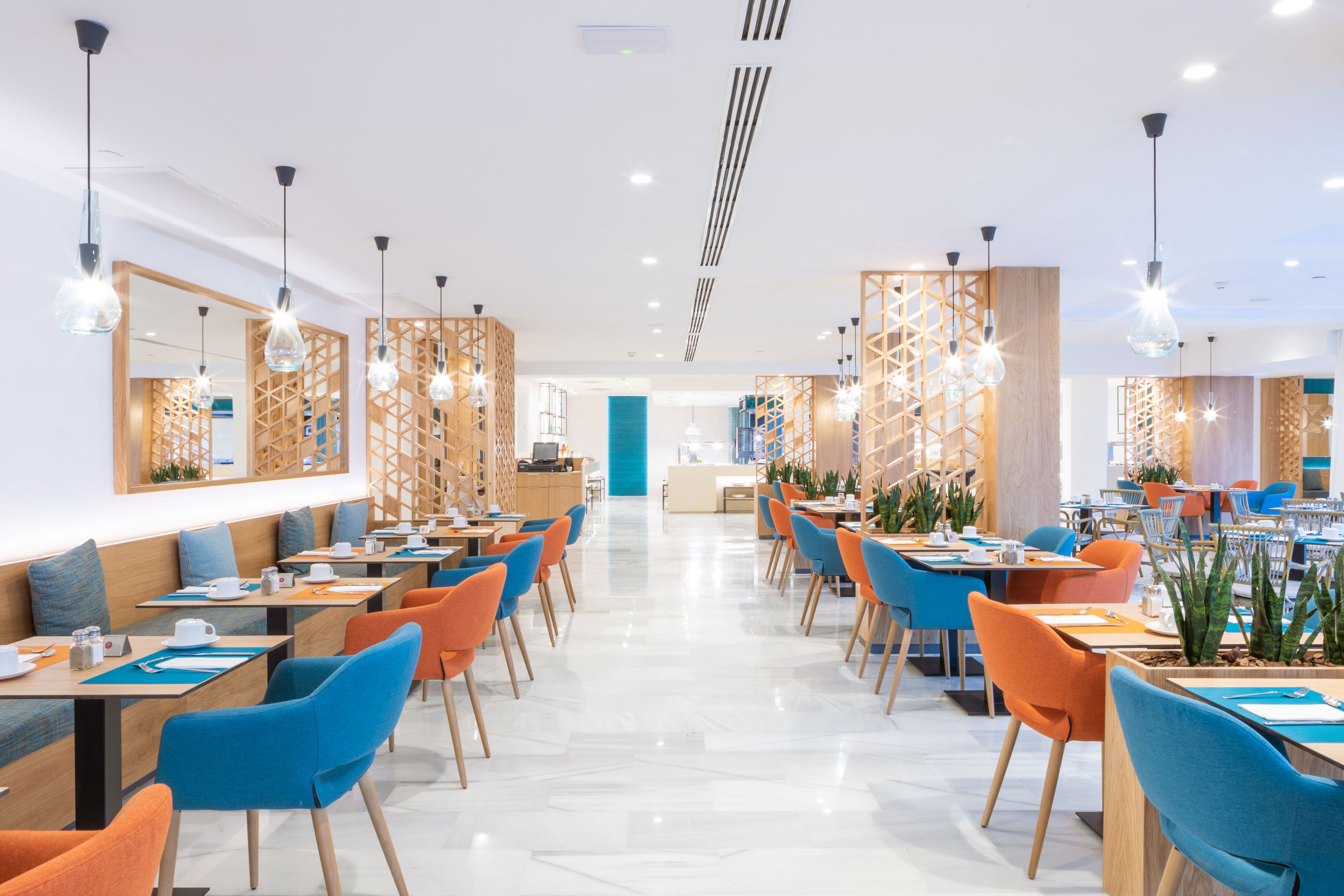 Un restaurant moderne avec des tables et des chaises hautes, un intérieur lumineux et un mur d’accent bleu au centre.