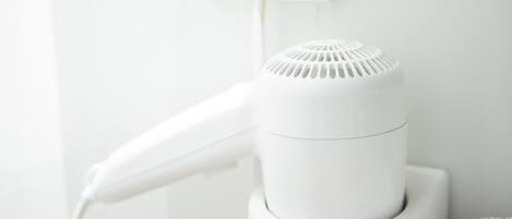 A white hair dryer mounted on a wall with a towel hanging nearby.