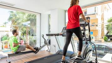 A gym with treadmills and a rowing machine, large windows, and a view of palm trees and buildings outside.