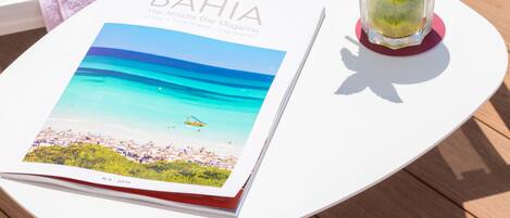 A white table with a magazine, a glass of iced drink with mint, and a towel with a logo.