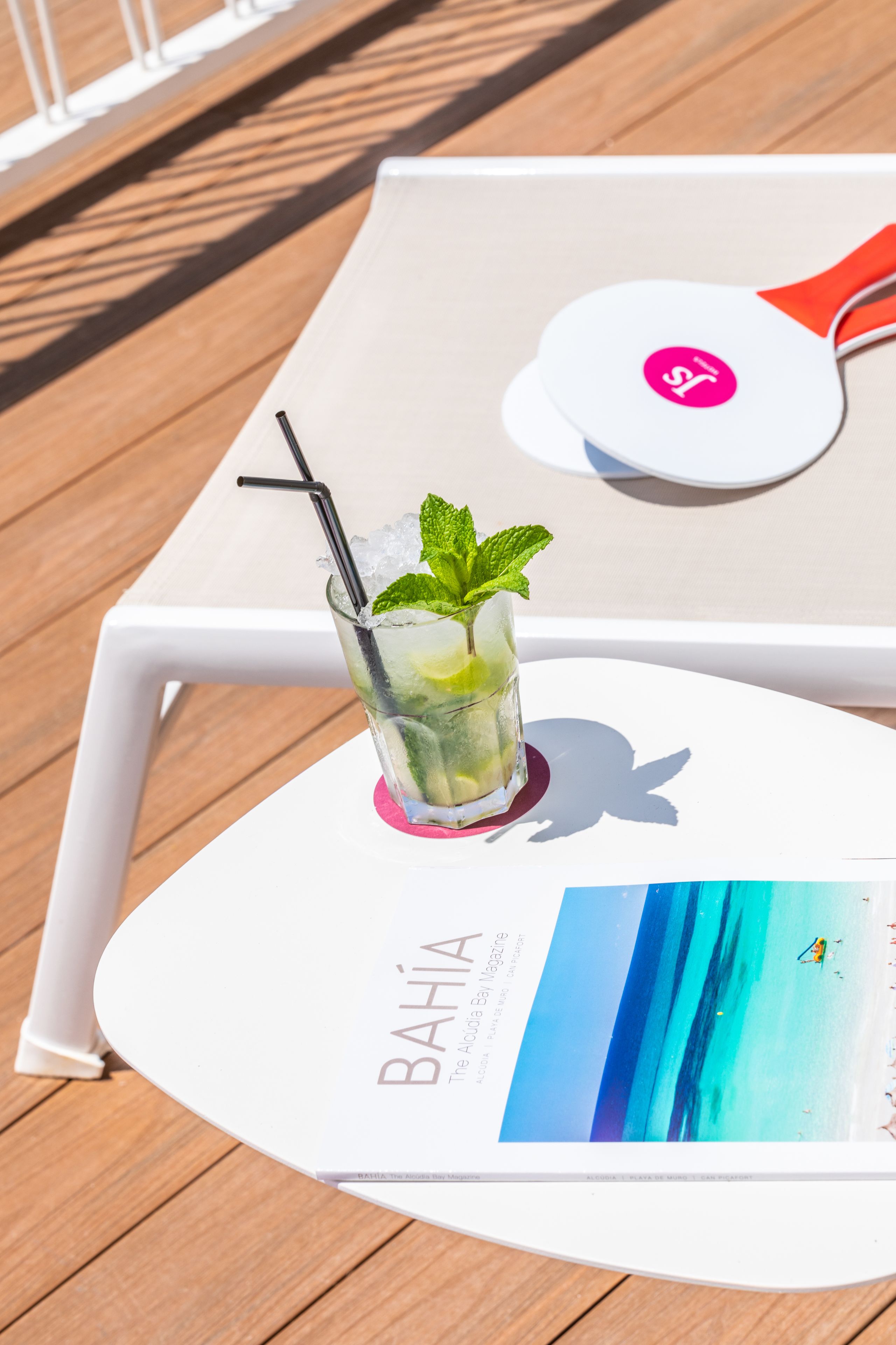 A glass of a refreshing drink with mint, ice, and a straw on a white tray with a magazine titled "BAHIA".