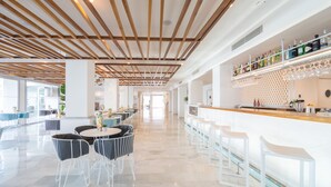 Un área de bar amplia y moderna, con una barra larga, taburetes y una gran variedad de botellas y vasos.