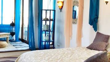 Un dormitorio con cama, cortinas, una lámpara de pared y vistas al exterior.