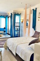 A bedroom with a bed, curtains, a wall-mounted light, and a view of the outside.
