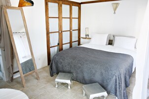 A bedroom with a bed, a wooden wardrobe, a nightstand, and a mirror.