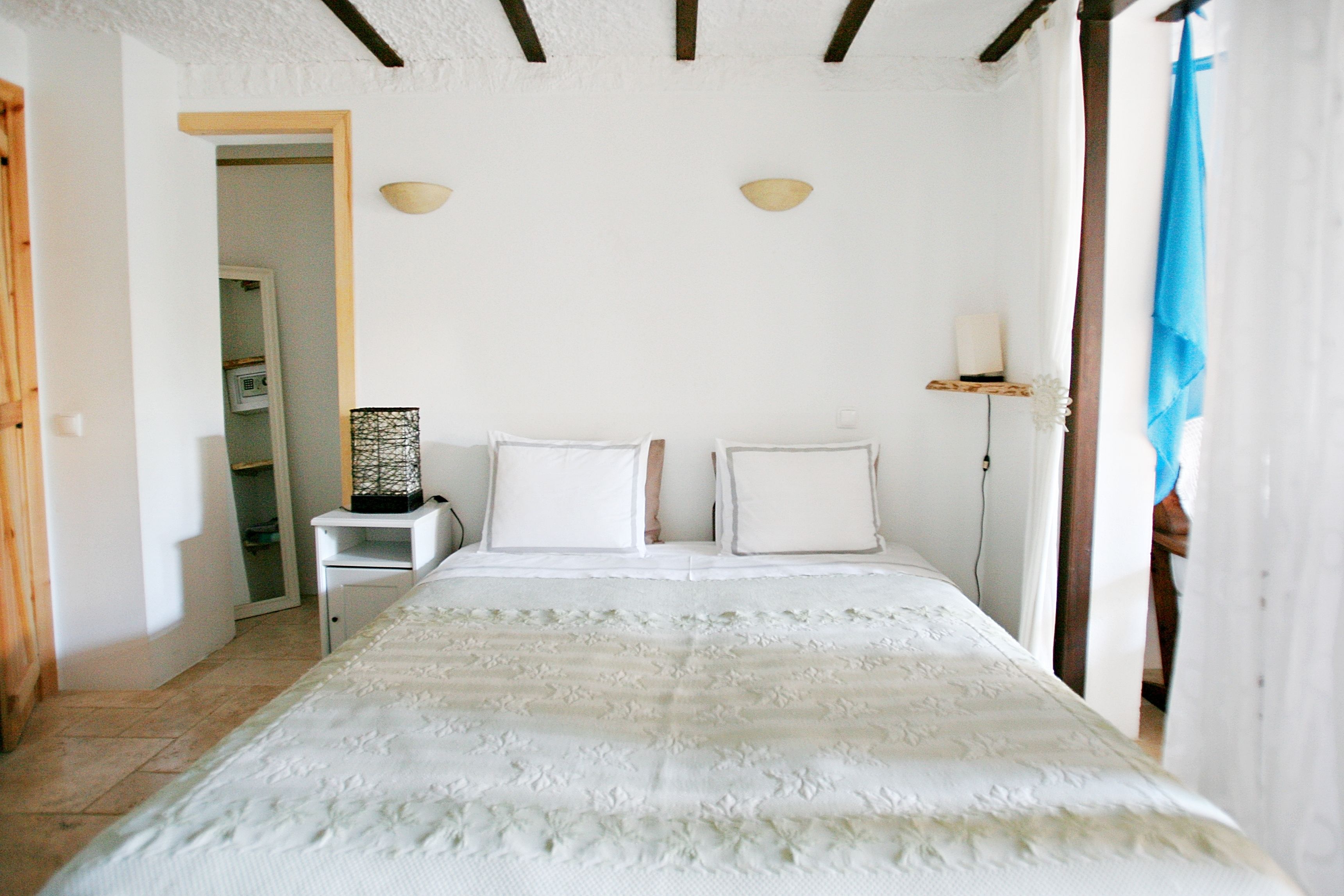 A bedroom with a large bed, a bedside table, a lamp, and a window with curtains.