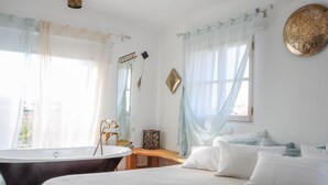 A bedroom with a large bed, a bathtub, and a wooden bench. - Uma Casa à Beira Sol (Lagos)