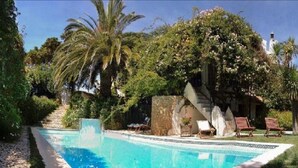 A swimming pool surrounded by palm trees and a stone structure. - Uma Casa à Beira Sol (Lagos)