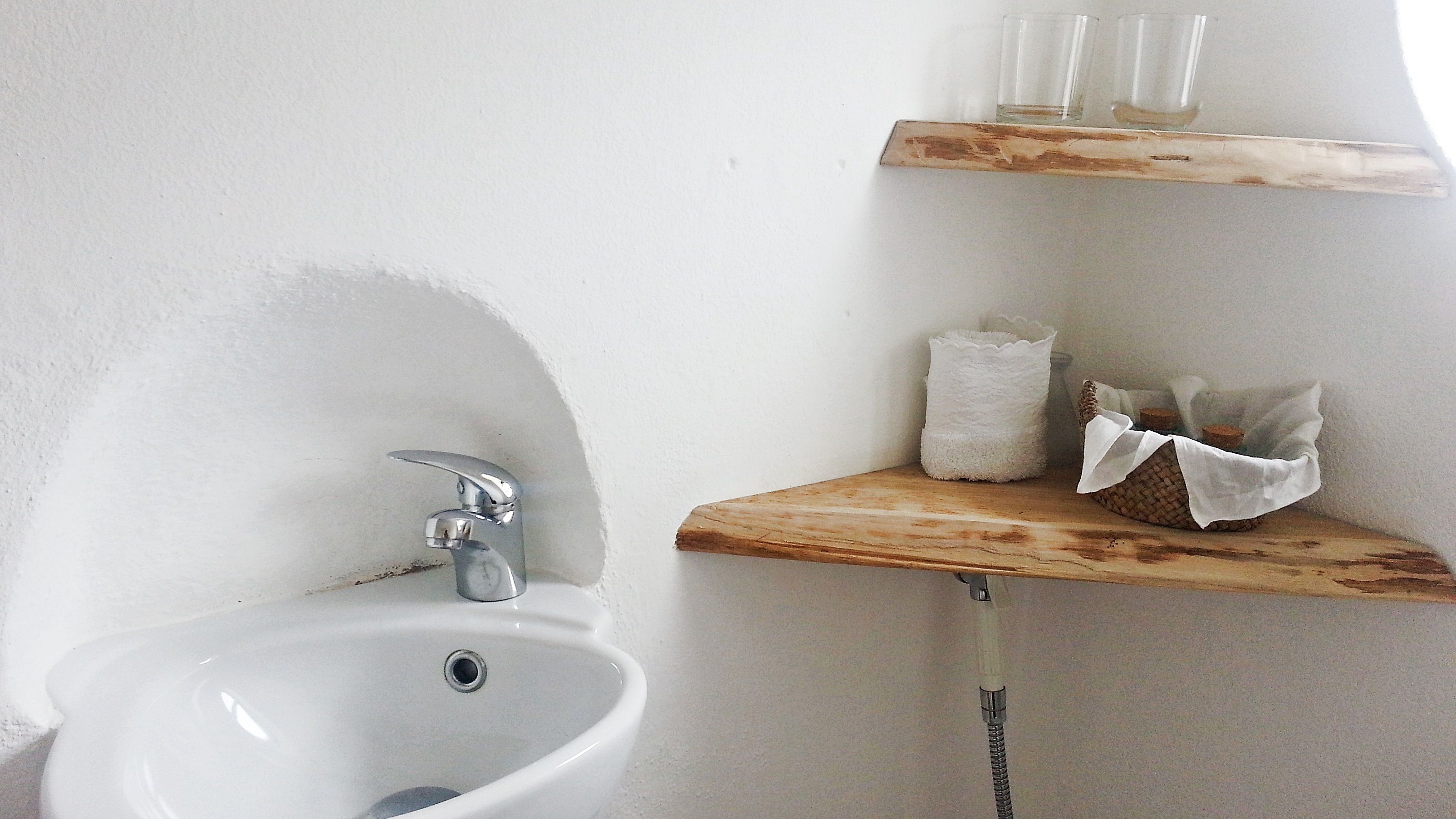 A bathroom with a white sink, a chrome faucet, and a wooden shelf holding a tissue box and a woven basket.