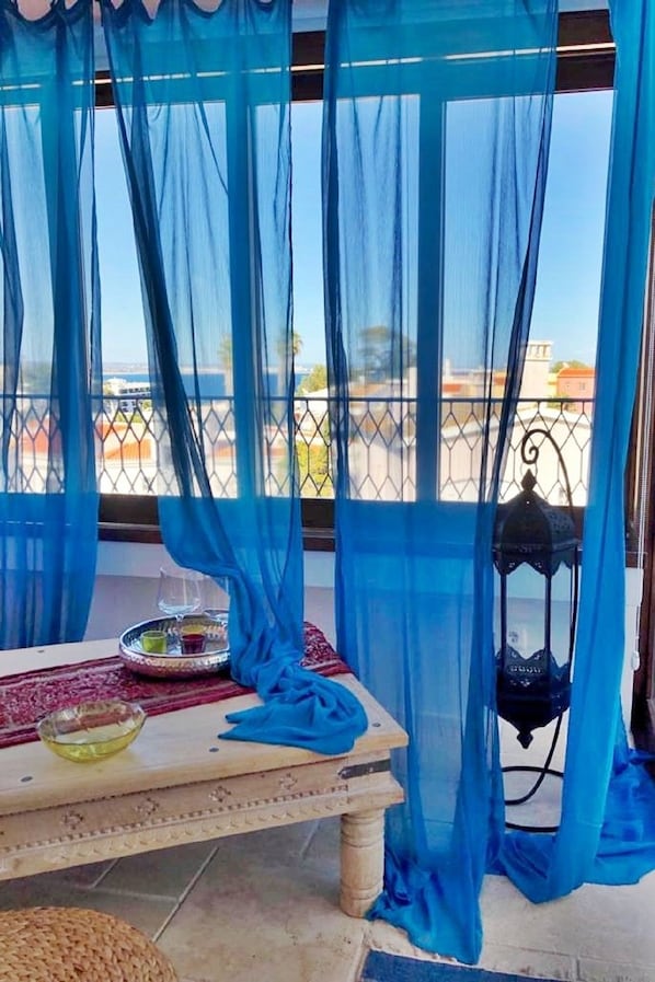 A balcony with blue sheer curtains, a table with a tray of glasses, and a lantern. - Uma Casa à Beira Sol (Lagos)